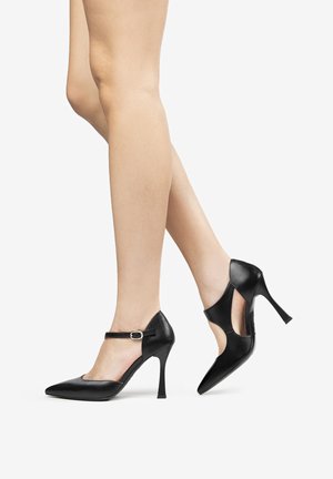 Tacchi alti neri in pelle con punte appuntite, cinturino alla caviglia e lati intagliati. Texture liscia con un design elegante e un tacco a spillo.