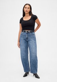 Must lõhestatud top lühikeste varrukatega, kombineeritud helesiniste kõrgvöökohal laia säärega teksadega. Viimistletud musta vöö ja terava ninaga saabastega.