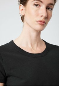 Juodasis medvilnės marškinėliai su apvalia iškirpte ir trumpomis rankovėmis. Audinys atrodo lygus su nedideliu blizgesiu, prigludusi dizaino.