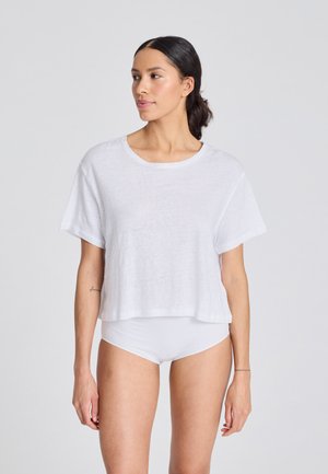T-shirt bianco corto con maniche corte, realizzato in tessuto leggero, con scollatura rotonda e vestibilità morbida. Indossato sopra della biancheria intima bianca.