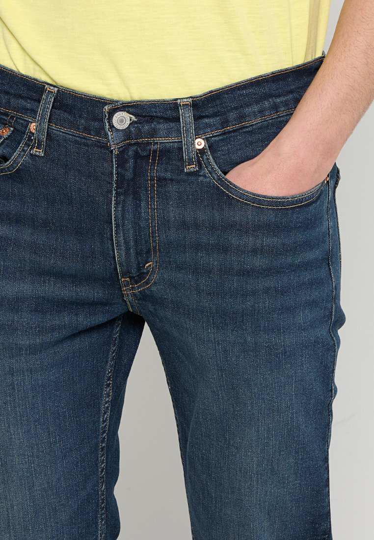 Dunkelblaue Jeans im klassischen Schnitt, mit Kupferbeschlägen, fünf Taschen und dezentem Verblassen. Der Bund ist standardmäßig mit Gürtelschlaufen ausgestattet.