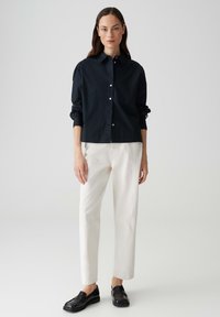 Navy button-up shirt with long sleeves, white casual trousers, and black loafers. Smooth fabric with a classic collar and cuff details.