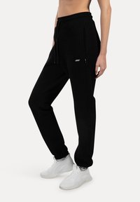 Sorte sweatpants med elastisk talje, snoretræk og sidelomme med lynlås. Fremstillet af blødt materiale, med slim fit og ribbede manchetter.