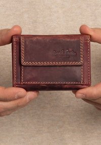 Portafoglio in pelle marrone con finitura texture, caratterizzato da una patta frontale, dettagli di cucitura e un logo impresso. Forma rettangolare compatta.