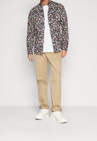 Chemise à motifs floraux avec fond noir, manches courtes et motifs de fleurs colorés. Associée à un pantalon beige clair et des baskets blanches.