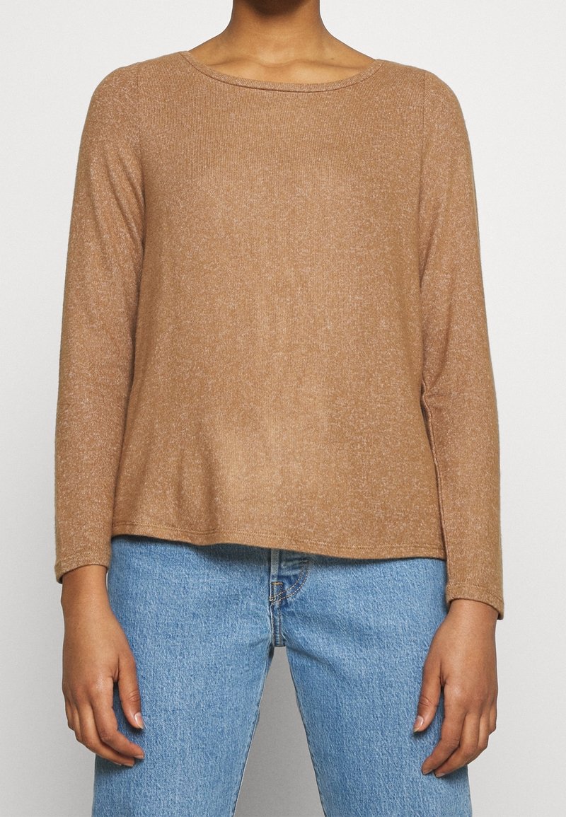 Pullover marrone a maniche lunghe in maglia testurizzata, con scollatura rotonda e orlo leggermente abbassato, abbinato a jeans azzurri chiari.