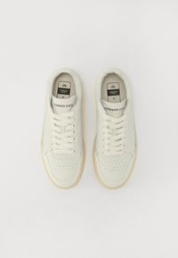 Hvite lær sneakers med perforert tåhette, flate snører og beige gummisåle. Merker på tungen leser "Copenhagen Studios" og størrelse 41.