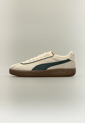 Μπεζ αθλητικό παπούτσι Puma με σκούρα πράσινη ρίγα και καφέ σόλα, χαμηλό σχέδιο, κορδόνια και λογότυπο Puma στο πλάι και στη σόλα.
