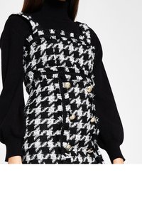 Schwarz-weißes Hahnentrapdesign-Kleid mit ausgefransten Kanten, goldenen Knopf-Akzenten und einer taillierten Passform; getragen über einem schwarzen Rollkragenpullover.