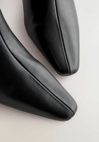 Sorte læder sko med spidse tæer og en glat overflade, der har diskrete syninger langs sømmene og en strømlinet form.