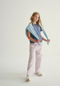 Neformální outfit skládající se z modrého trička s krátkým rukávem, pruhovaných růžových a bílých kalhot a bílých tenisek s hnědou podrážkou. Světle modrá mikina přehozená přes ramena.