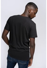 Sort bomulds t-shirt, korte ærmer, rund halsudskæring, lidt længere bagkant, parret med blå denim jeans. Minimalistisk design, blød tekstur.