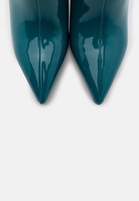 Zapatos de tacón alto de charol verde azulado con un diseño de punta afilada y acabado sin costuras. La textura brillante acentúa la silueta estilizada.