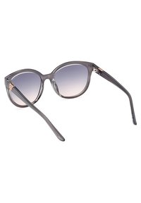 Gafas de sol de plástico gris con forma de ojo de gato, con lentes degradados y varillas delgadas. Acento notable en el área de la bisagra.