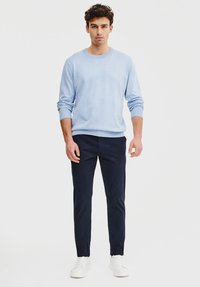 Jasnoniebieski sweter z okrągłym dekoltem, granatowe spodnie slim-fit i białe sneakersy. Miękka tkanina, ściągacze oraz minimalistyczny design. Gładkie tło.