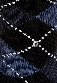 Suéter de punto con un patrón de diamantes en azul marino, negro y blanco. Presenta un pequeño logo redondo en la parte inferior izquierda.