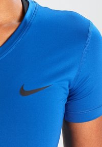 Primer plano de una persona que lleva una camiseta de deporte de manga corta azul de Nike con el logotipo en forma de swoosh negro en el pecho.