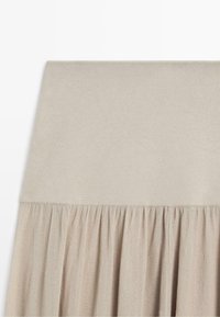 Beige rok met een brede tailleband en geplooide stof eronder, die een zachte, vloeiende textuur creëert.