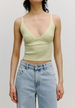 Lichtgroen geribbeld tanktop met een V-hals ontwerp, gecombineerd met hooghangende lichtblauwe denim jeans, die een getailleerde silhouet laat zien.
