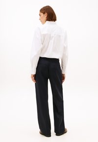Biała koszula z falbaniastym kołnierzykiem połączona z granatowymi, szerokimi spodniami. Ubranie ma dopasowany krój i gładką teksturę, z subtelnymi detalami z tyłu.