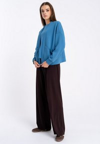 Niebieska, oversize bluza z luźnym krojem, z przednimi kieszeniami i ściągaczami na rękawach, w połączeniu z szerokimi brązowymi spodniami i brązowymi butami.