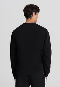 Felpa nera con scollatura a girocollo, polsini e fondo a coste. Texture liscia, design semplice, senza loghi o motivi visibili. Vista posteriore mostrata.