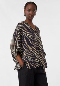 Camicia ampia in tessuto navy scuro con un sorprendente motivo a strisce tigre beige. Caratterizzata da un collo a V e dettagli con bottoni sul davanti.