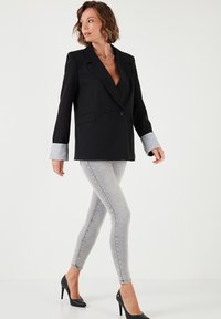 Černý dvouřadý blazer s šedými manžetami, zkombinovaný se světle šedými skinny džínami a černými vysokými podpatky, s hladkou texturou a přizpůsobeným střihem.