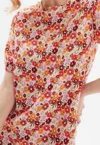 Haut floral avec un fond rose orné de fleurs rouges, oranges et lilas. Manches courtes bouffantes et coupe ample. Tissu léger avec une texture douce.