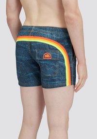 Costumi da bagno in denim con un accento laterale a strisce arcobaleno, dotati di tasca posteriore, vita piatta e tessuto blu testurizzato. Logo visibile sulla tasca.