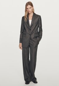 Dark grey tailored suit with a single-breasted blazer featuring two front pockets and matching wide-leg trousers. Smooth fabric texture.