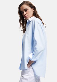 Lichtblauw gestreept shirt met een witte kraag, lange mouwen opgerold bij de manchetten en een relaxed fit. Opvallende zijsplitten aan de onderrand.