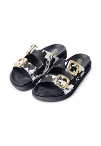 Black and white cow-print slide sandals with two gold buckle accents, featuring a textured black sole and an open-toe design.