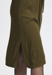 Olivno zelena obleka do kolen z teksturiranim materialom, ki ima odprtino na hrbtu in zavezovanje v predelu pasu.