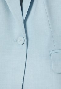 Veste bleu clair avec un bouton unique recouvert de tissu et une petite poche passepoilée sur le côté droit.