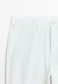 Hvide bukser med sidelommer, bæltestropper og knaplukning i taljen, vist forfra på den øverste halvdel.