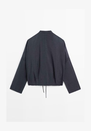 Ciemnoszara kurtka o luźnym kroju, z długimi rękawami, wysokim kołnierzem i ściągaczem u dołu, pokazana od tyłu na białym tle.