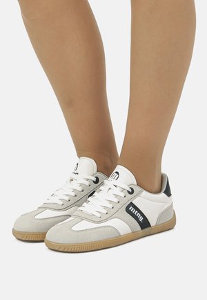 Zapatillas con una combinación de gamuza gris y cuero blanco. Presentan una raya de acento negra y una suela de goma texturizada. Los cordones son blancos.