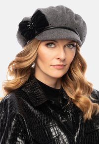 Grau gefilzte Mütze mit schwarzem Blumenakzent, verziert mit Perlen; Model trägt eine glänzende schwarze Kunstlederjacke.