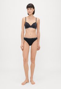 Black lingerie set featuring a sparkly bralette with thin straps and matching black panties with a logo waistband. Minimalistic design.