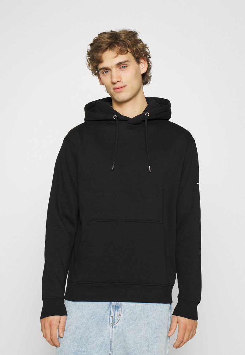 Sort hættetrøje med lynlås og lomme foran, snoretræk og ribbede manchetter, iført med lyseblå denimshorts. Enkel, pullover-design.