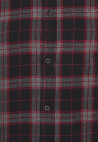 Camicia di flanella a scacchi rossi e grigi con uno sfondo nero, dotata di bottoni e una texture morbida. Classico motivo a quadri con colori a contrasto.