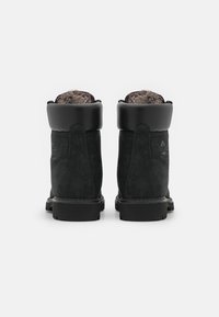 Botas de ante negras con detalles de cuero, forro de piel y una suela de goma gruesa. Presentan una punta redonda y un tacón ligeramente elevado.