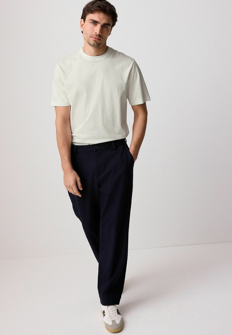 Lysegrå tekstureret t-shirt parret med navy bukser og hvide sneakers. Skjorten har et minimalistisk design med korte ærmer og rund halsudskæring.