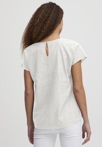 Blusa bianca in lino con maniche corte, scollatura tonda sul retro e dettaglio a chiave. Il tessuto ha una finitura testurizzata e una vestibilità comoda.