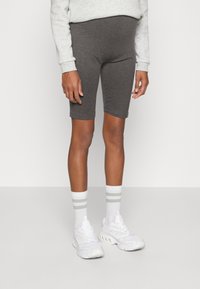 Szare shortsy rowerowe z bawełny z elastycznym paskiem w talii, zestawione z białymi sneakersami i pasiaste skarpetki typu crew. Gładka tekstura i dopasowany krój.