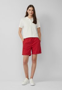 Witte polo, rode shorts met opgerolde mouwen, elastische tailleband en witte sneakers. Eenvoudige, casual outfit met een strak design.