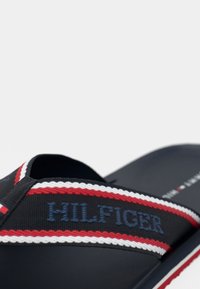Navy slide sandal with textile strap featuring red and white braided accents and "HILFIGER" in blue, rubber sole, open-toe design.