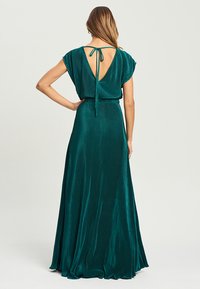 Robe maxi teal avec un détail de nœud à l'arrière. Dispose d'un dos en V profond, de manches courtes et d'une texture plissée pour un look élégant.