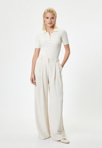 Witte geribde poloshirt met korte mouwen, voorzien van een kraag en knoopsluiting aan de voorkant. Gecombineerd met crèmekleurige, hoge brede broek.